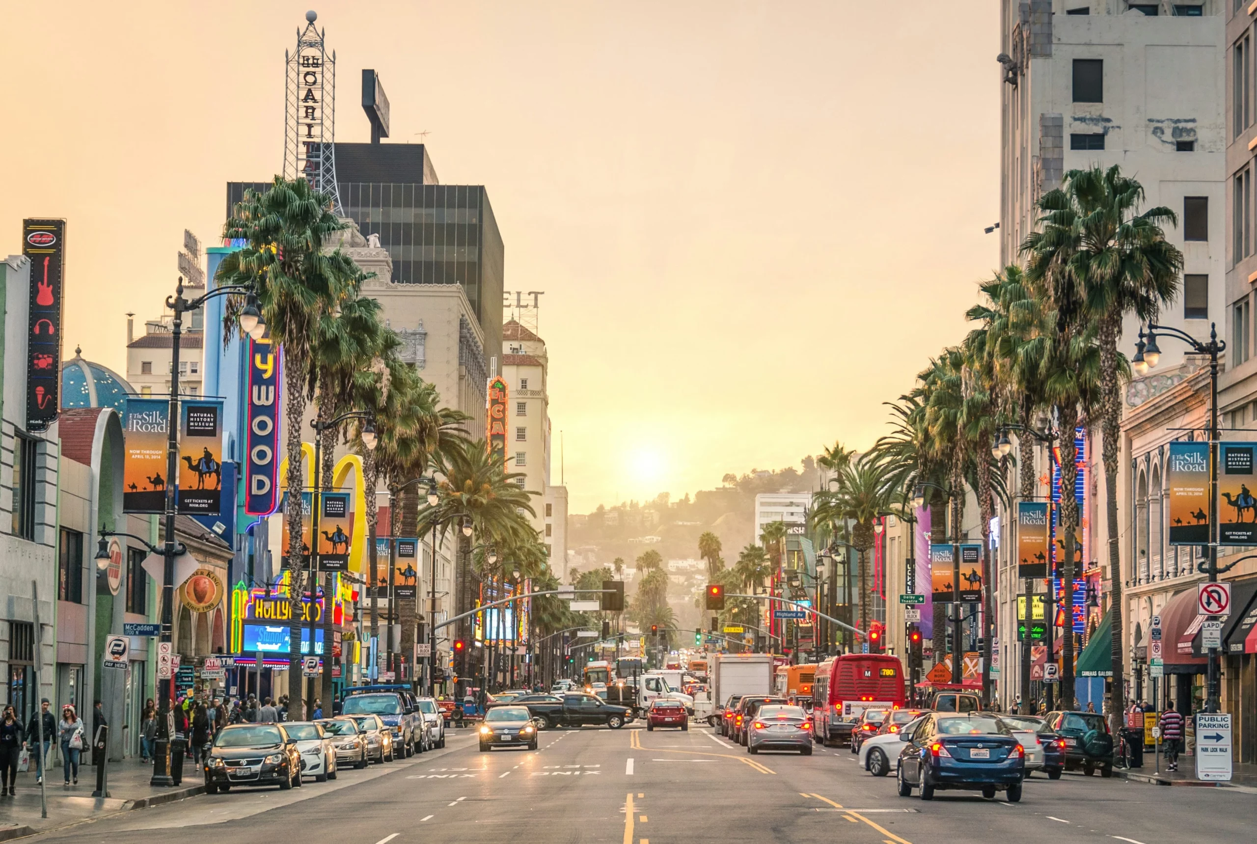 A view of sunset boulevard with flashy neon signs and palm trees at sunset. All of these businesses consult with specialists about California moving expenses before relocating there.