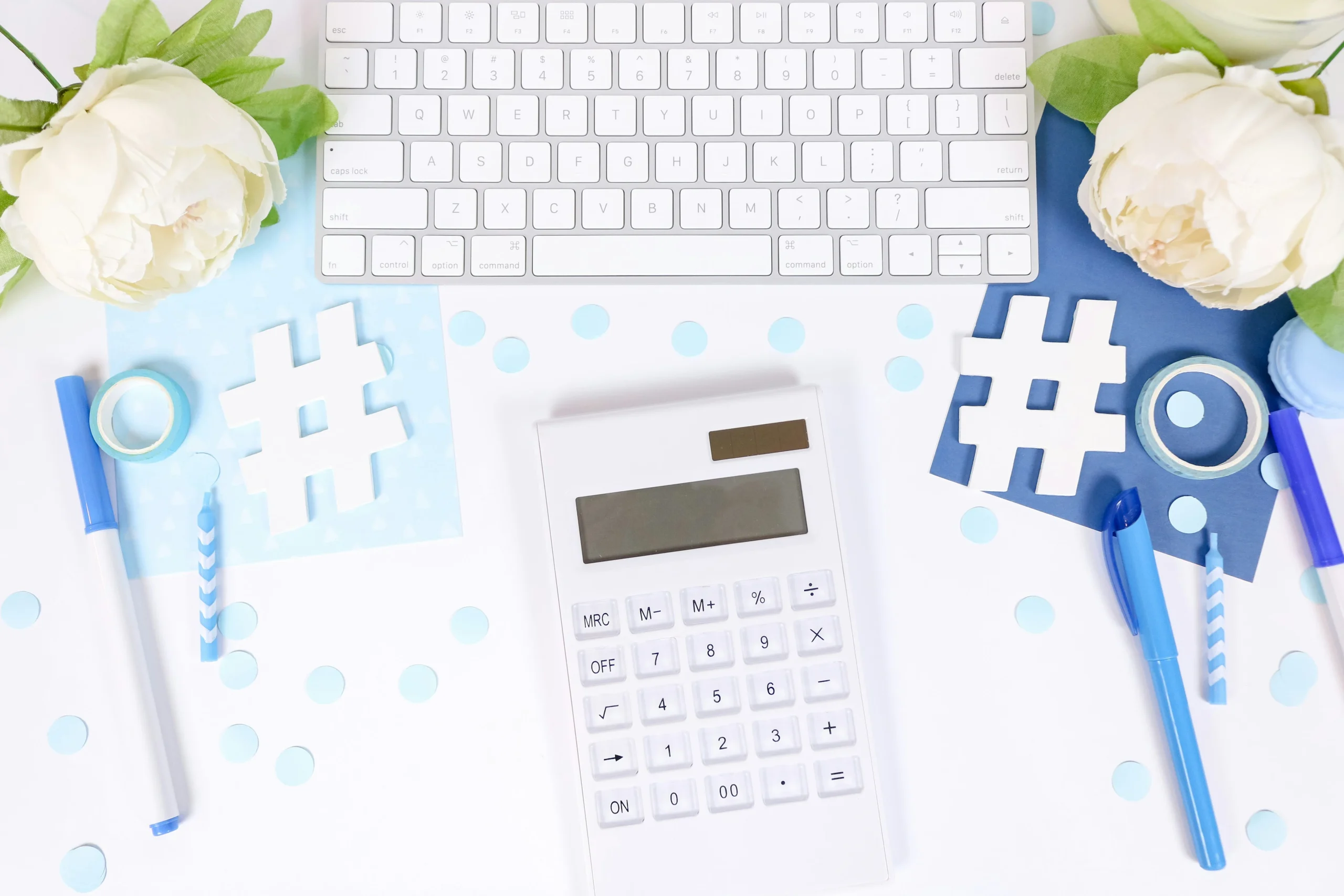 a calculator and some stationary are near a computer keyboard. white hashtags are laying on top. these objects symbolize remote accounting services.