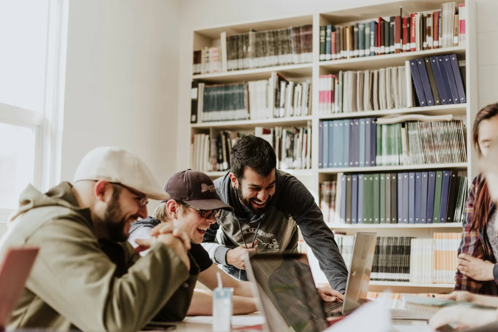 A group of young professionals gather around some laptops in an office space, excited to get bookkeeping services for startups.