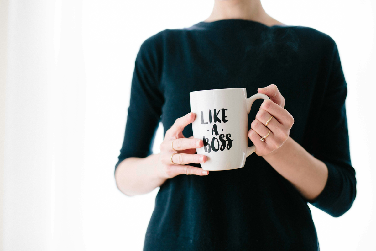 A woman in a black shirt, whose face is not in the frame, is holding a white mug that says, "Like a boss." in black text on the front.