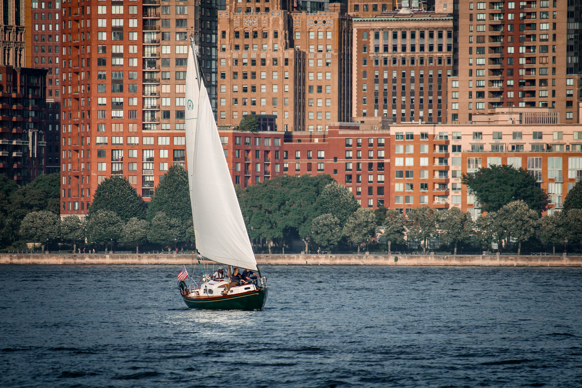 The waterfront in Jersey City, with a sailboat going across the front of the skyline. Find the best CPA Jersey City has to offer remotely.