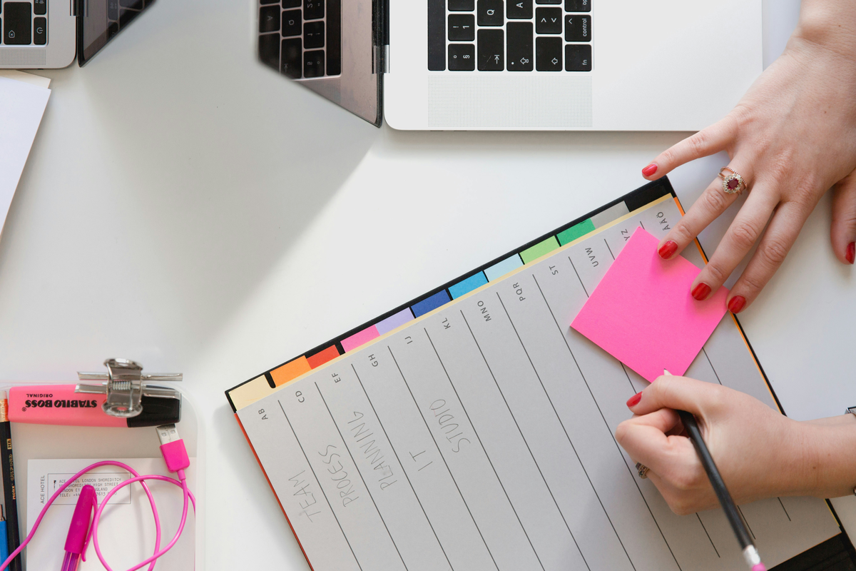 Someone has a laptop and stationary on their white desk. Their hands are holding a sticky note. They are about to research production accounting software before finding affordable remote CPAs instead.