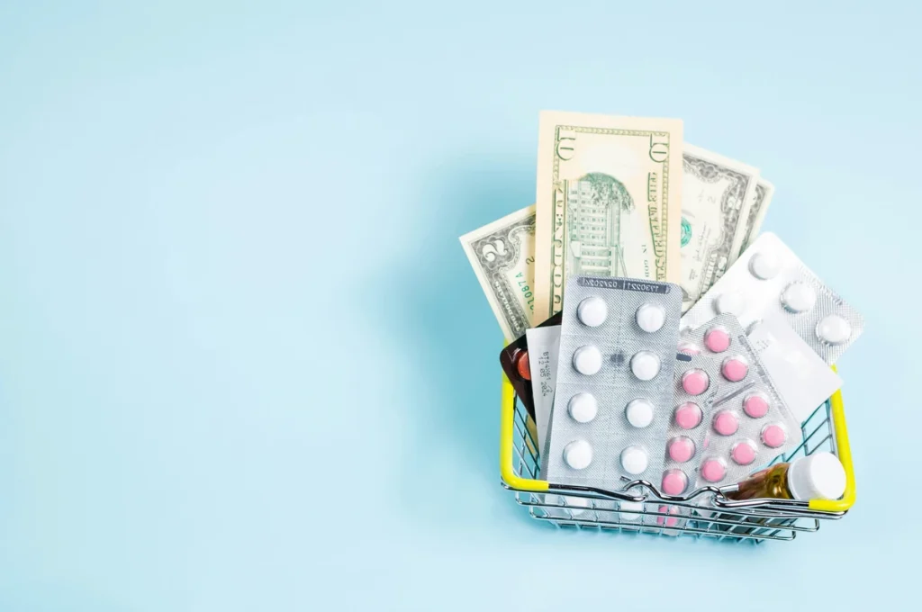 Medications in a pile with some cash over a light blue background.