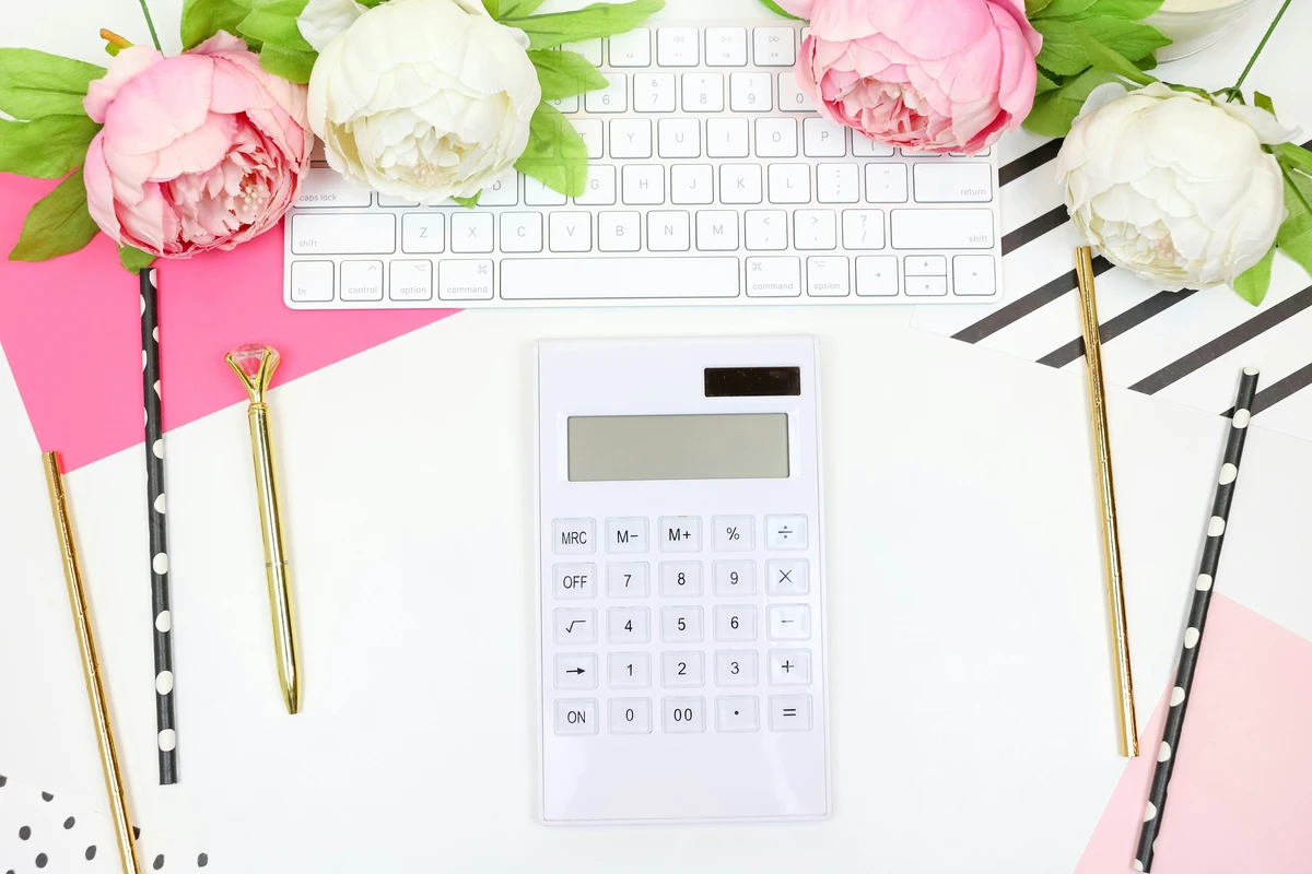 A white calculator on a white desk, also with a white keyboard, pink envelope, pink and white flowers, and various stationary like pencils. This is what you need in front of you when searching 'how do I report a 1099-s on my tax return'.